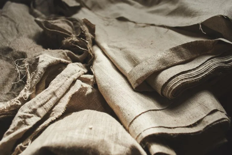 Stacked natural linen fabric in earthy tones showing traditional textile texture and raw fiber material
