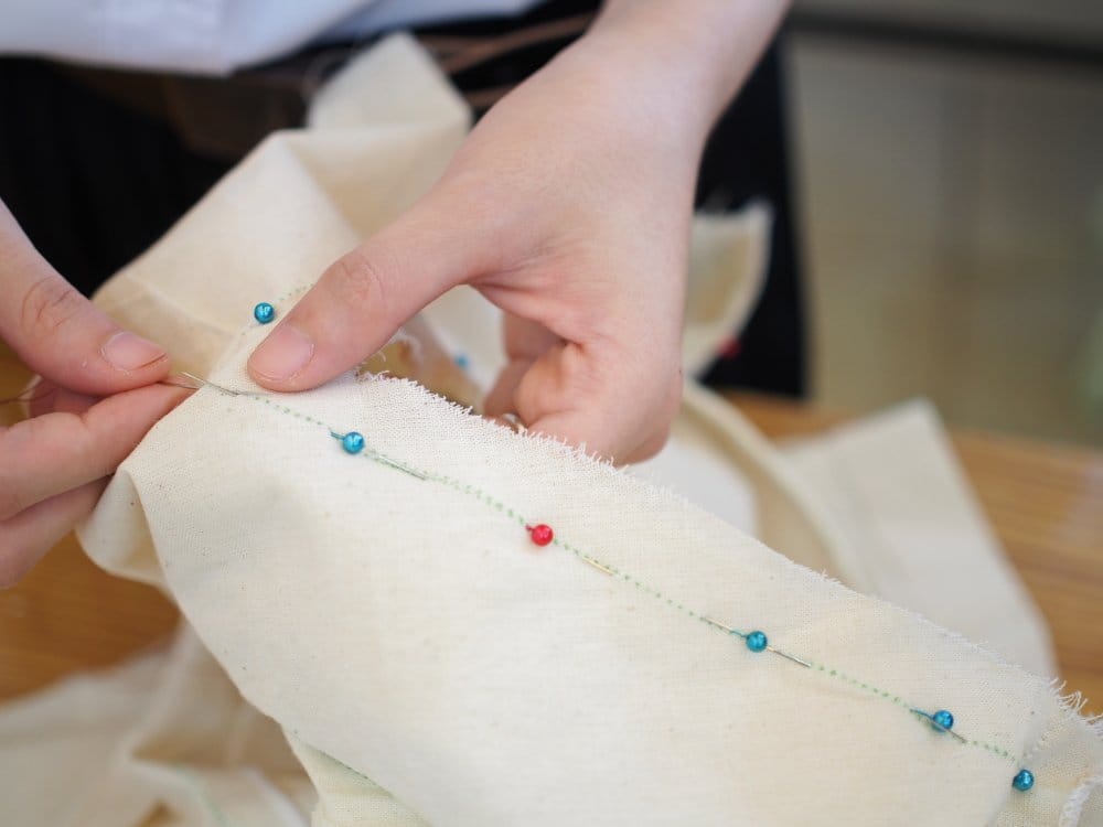 Hands pinning fabric with sewing pins demonstrating fabric finishing techniques