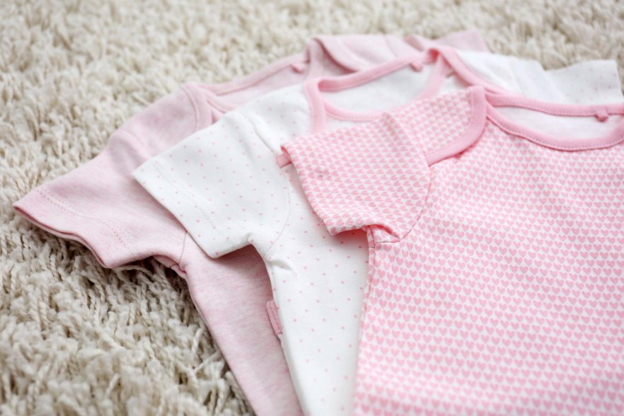 Essential baby clothes laid out including onesies, sleepers, and basic garments for newborns