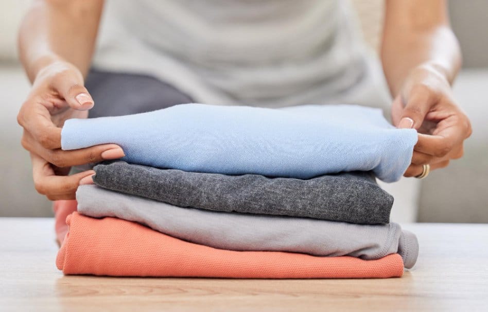 Hands folding clean clothes on table for proper fabric care