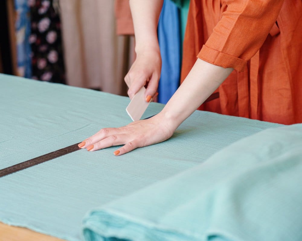 Measuring and cutting fabric on a table using ruler and fabric cutter
