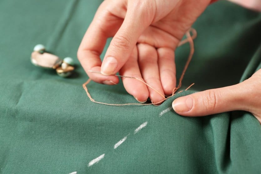 Close up of hand sewing straight stitches on green fabric with needle and thread