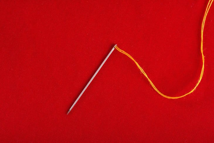Needle threaded with doubled thread on red fabric background