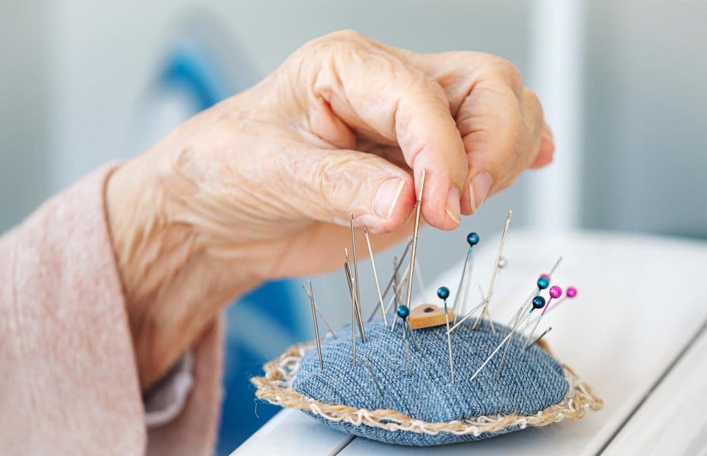 Older adult hand selecting sewing needle from pin cushion