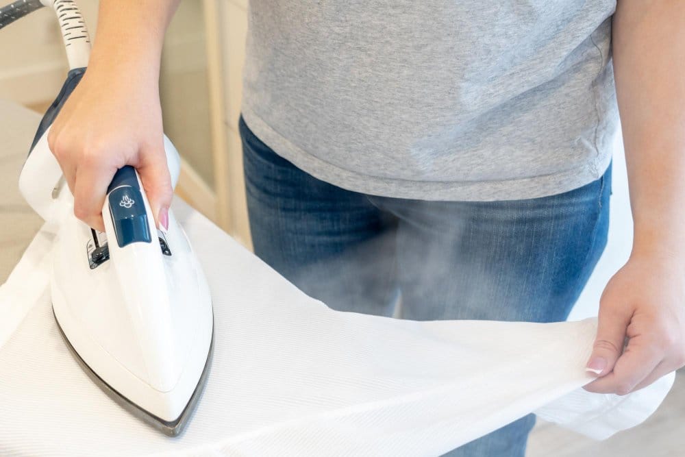 holding a steaming iron over a wrinkled linen clothe on an ironing board