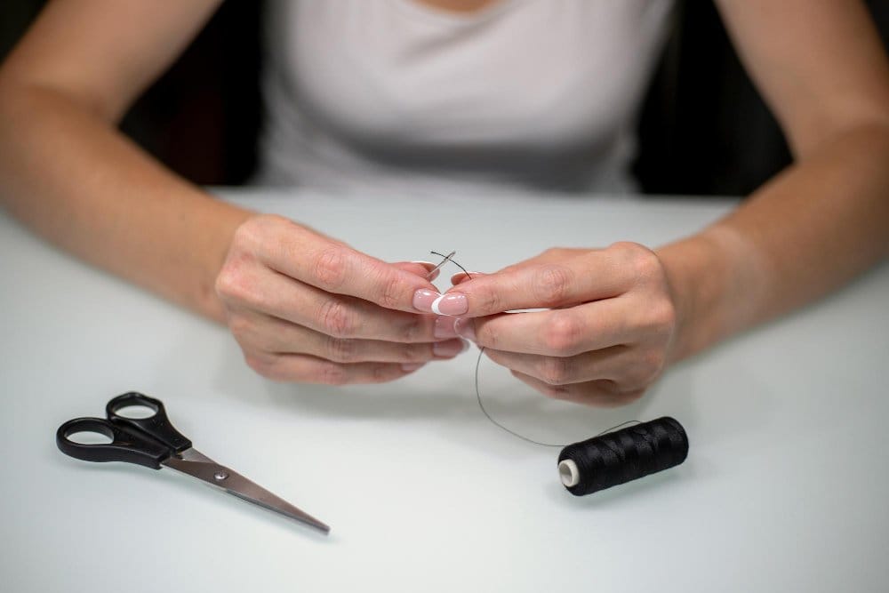 Sewing tools including scissors, needles, thread, and white card for threading setup