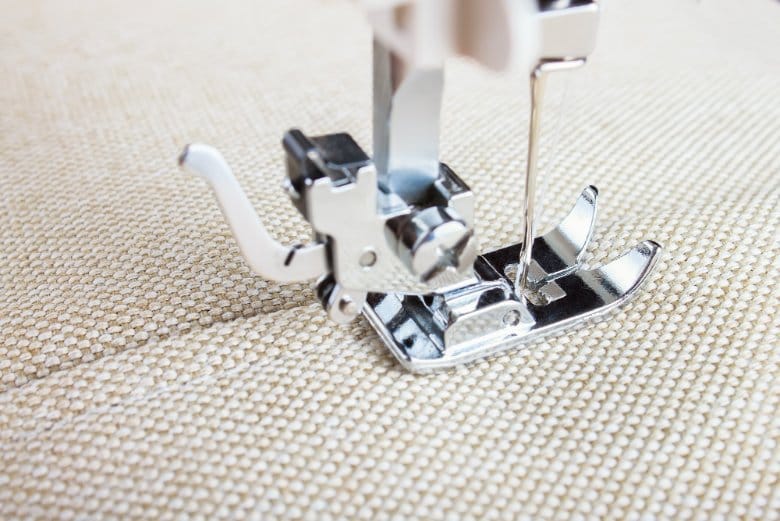 Close up of sewing machine presser foot positioned for straight stitch on fabric