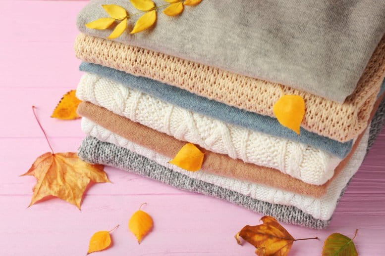 Stack of folded knit fabrics with autumn leaves representing seasonal textile choices