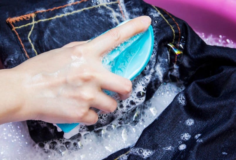 denim jeans being hand washed in soapy water with a soft brush