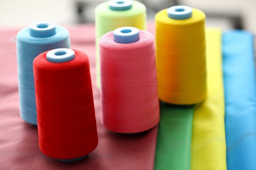 Colorful sewing thread spools arranged on fabric background