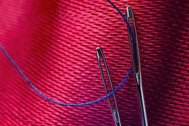 Close up of sewing needles and thread against textured fabric background