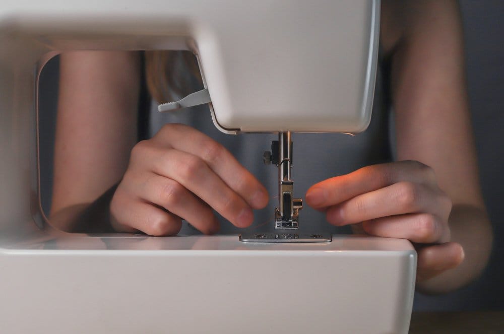 Hands guiding thread through sewing machine needle and presser foot