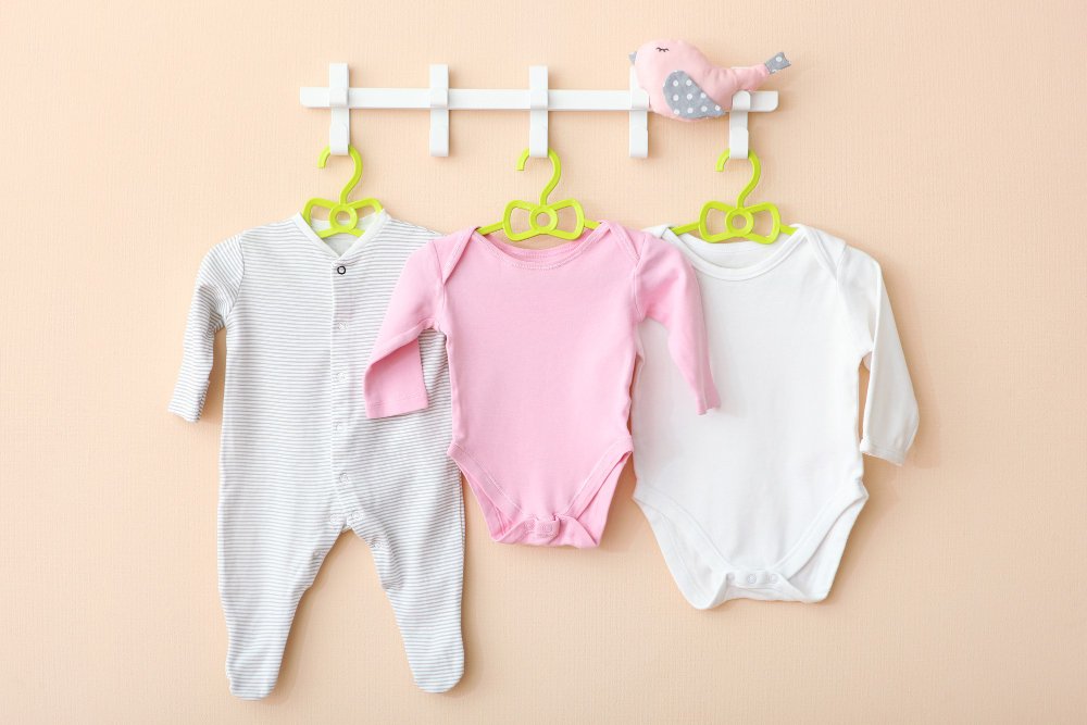 Essential baby wardrobe items laid out including onesies, sleepers, and seasonal clothing
