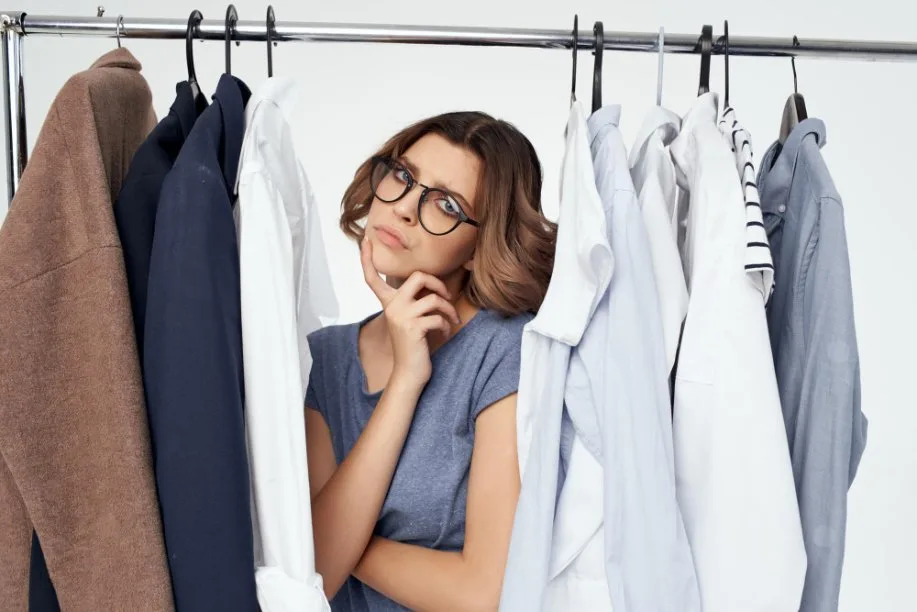 Woman standing between clothing rack analyzing garment fabric types and questioning clothing fiber content