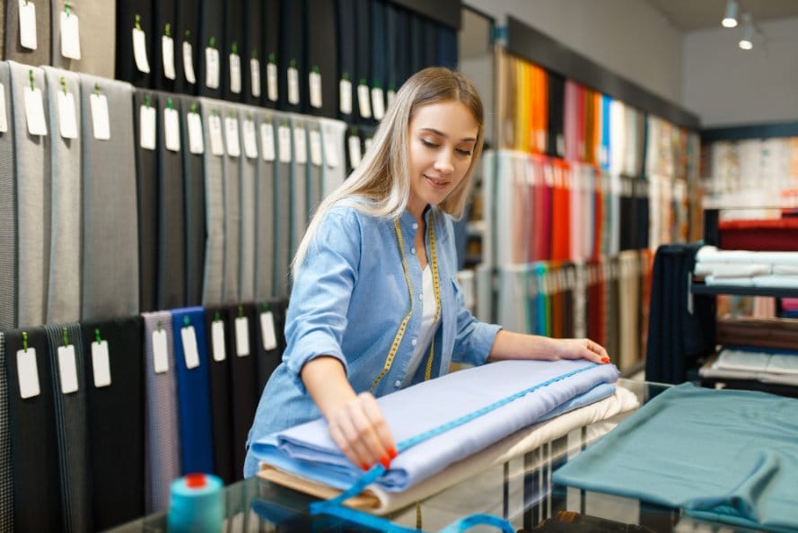 Woman measuring blue fabric in fabric store while shopping for trending textiles
