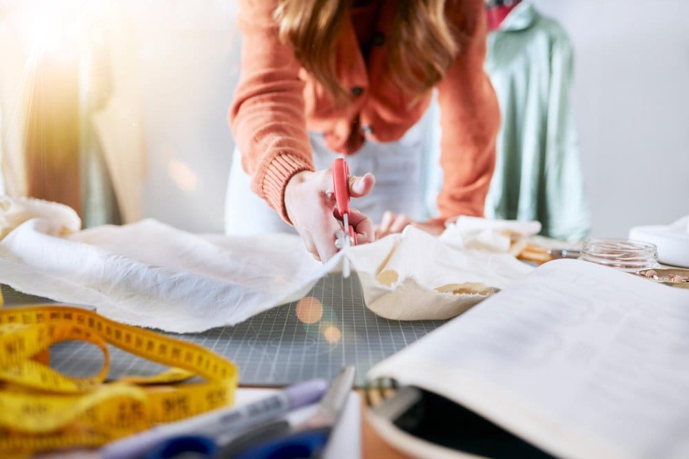 beginner cutting fabric with scissors on cutting mat while working on first sewing project