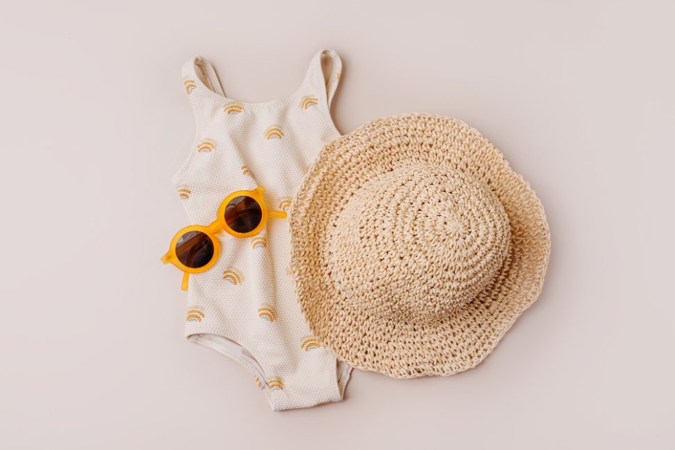 Collection of summer baby essentials including cotton onesies, sun hats, portable fan, and cooling accessories