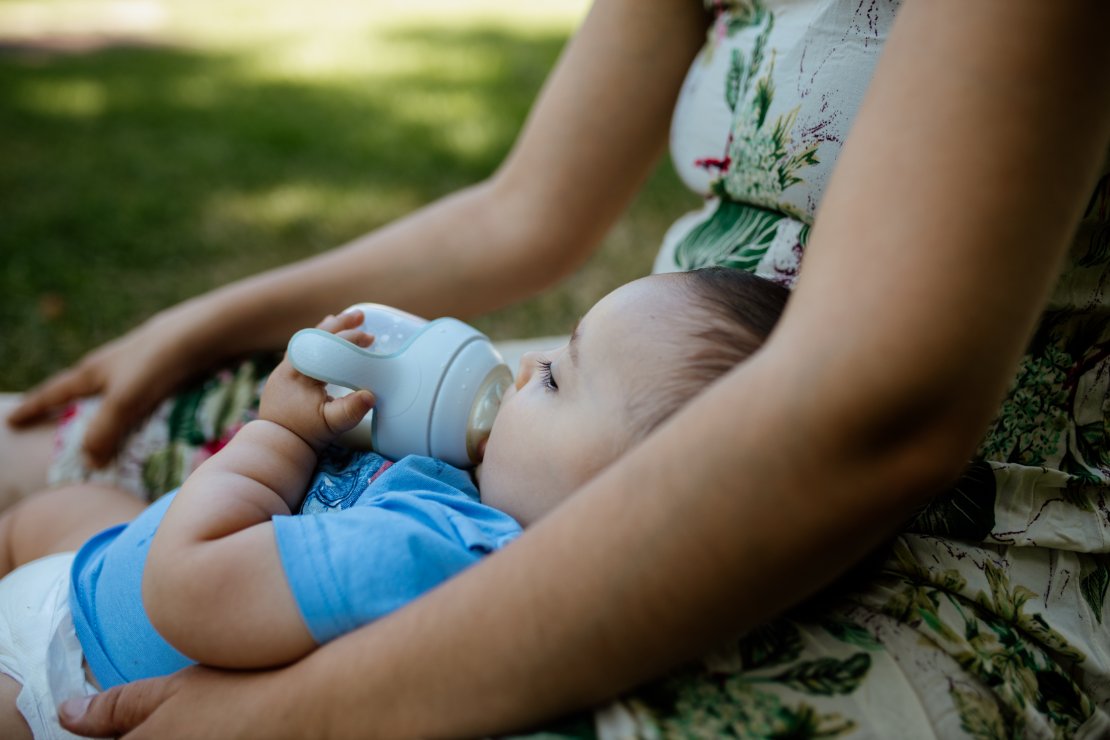 Mother breastfeeding baby in cool environment with water bottle nearby showing proper hydration during summer