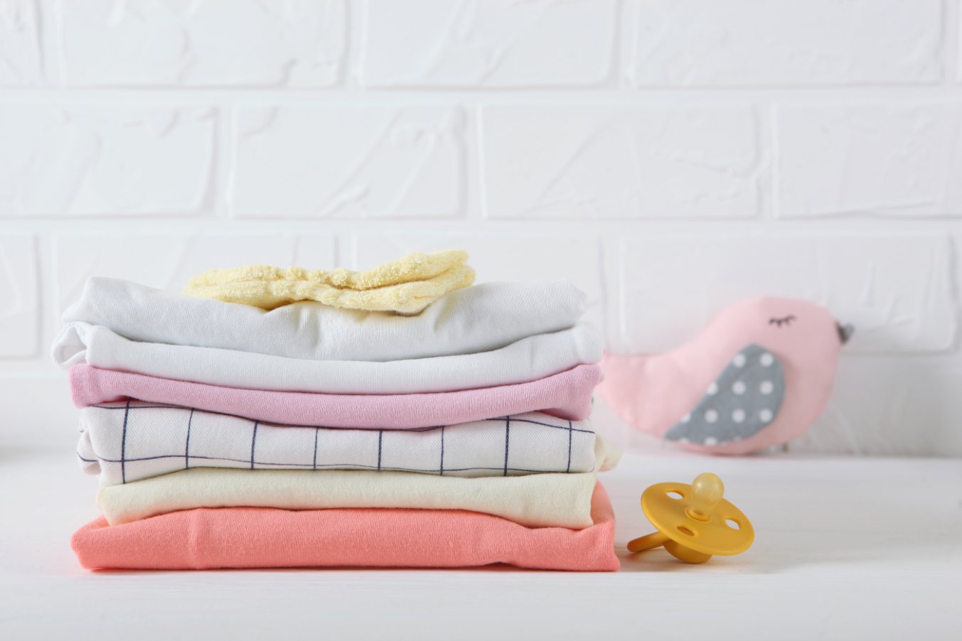 Stack of colorful newborn onesies arranged on a clean white surface with various patterns