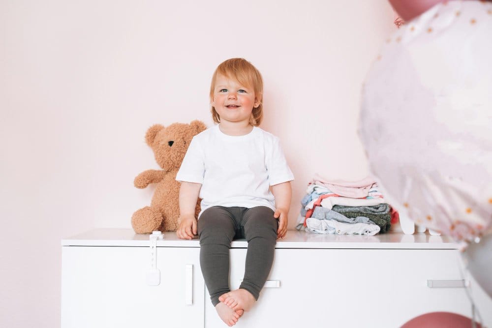 A smiling toddler sitting on a cupboard at home