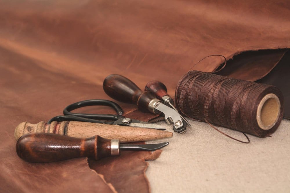 Leatherworking tools with thread, awls, and scissors on natural hide