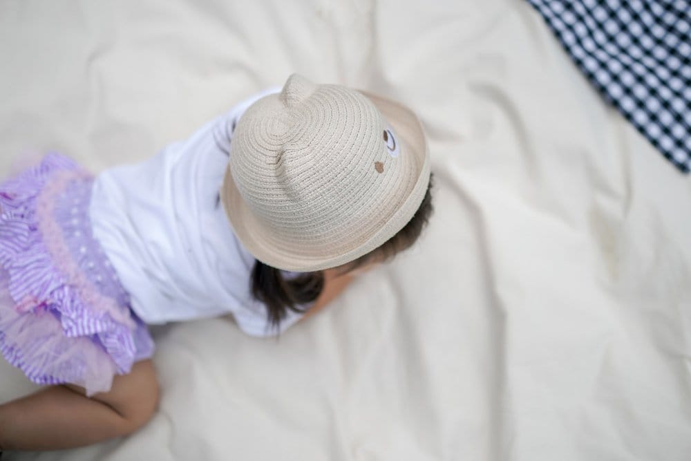 Toddler girl with her hat is crawling on the cream cloth