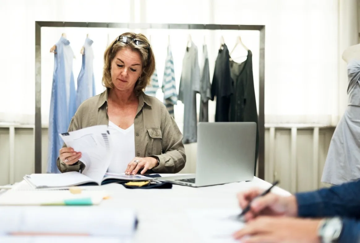 Fashion professional reviewing clothing documents and cost reports at desk