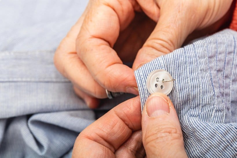 Hand sewing white shirt button back on striped fabric
