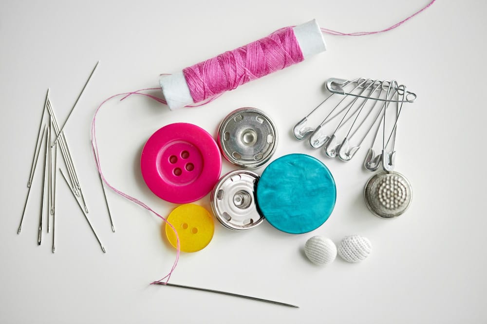Needles thread buttons safety pins and sewing tools on white background