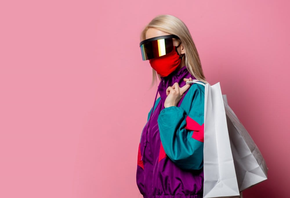 Blonde woman in 80s clothes wearing a face mask and futuristic looking glasses holding shopping bags