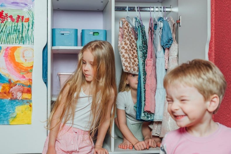 Children playing and having fun hiding in a closet with clothes