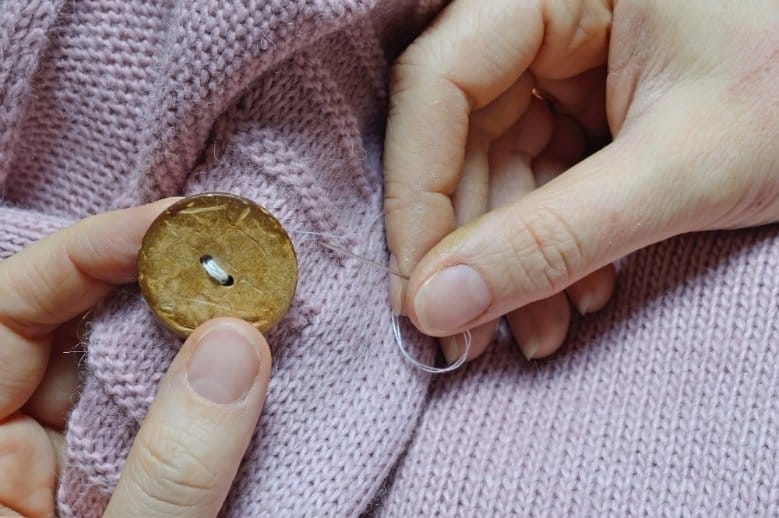 Female workers' hands sew a wooden button to a jacket
