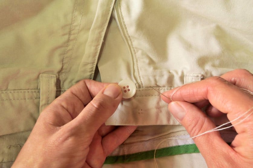 Someone attempting to stitch a button on a pant