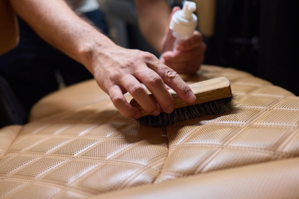 Person brushing quilted leather upholstery while applying conditioner