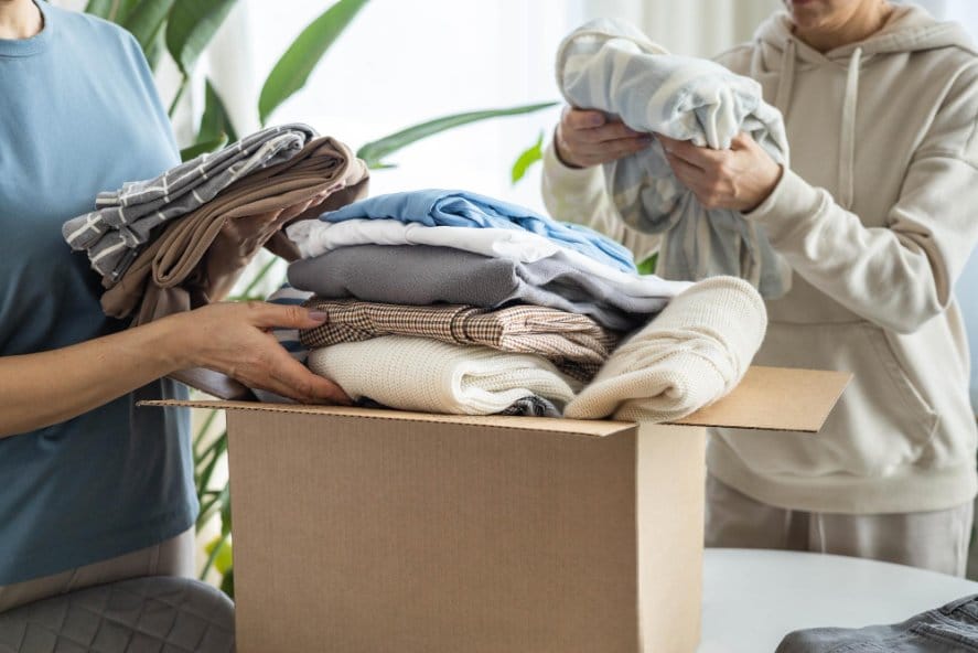 People sorting folded clothes into donation or resale box
