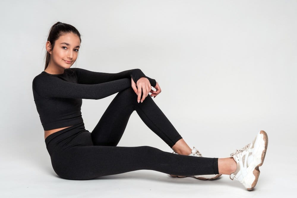 A woman sitting on the floor wearing a black activewear made with stretchy fabrics