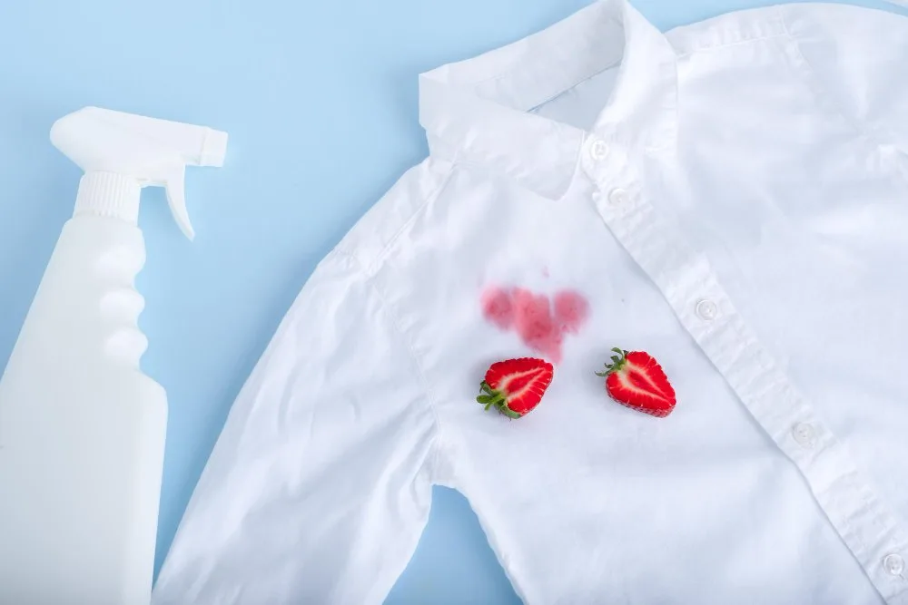 a stained white shirt on the floor with strawberry and stain remover spray