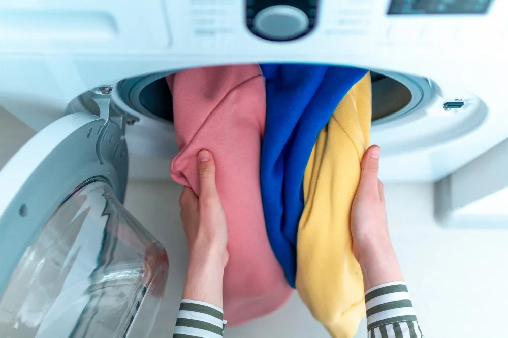 Loading colored active clothes in washing machine, doing laundry at home