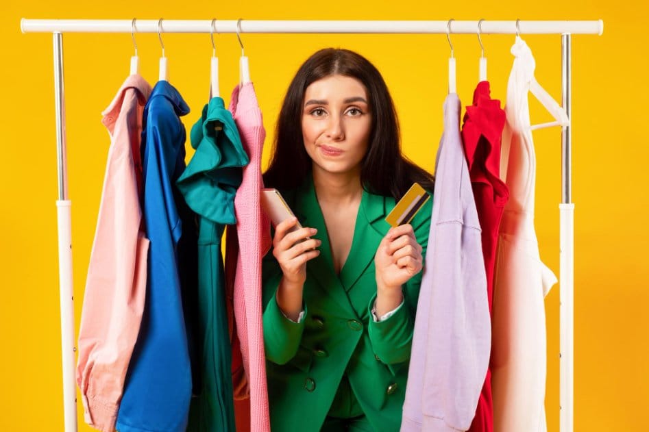 Woman holding credit cards while standing between colorful clothing rack