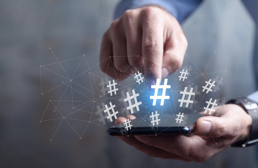 Hand using smartphone with floating hashtag social media icons