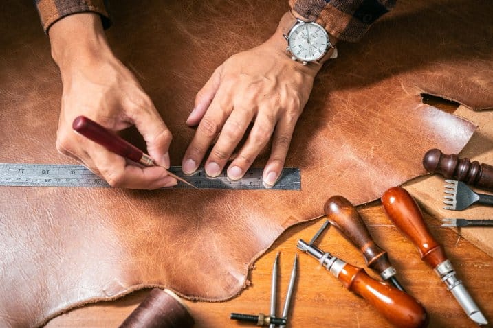 Craftsperson marking leather hide with ruler before restoration work