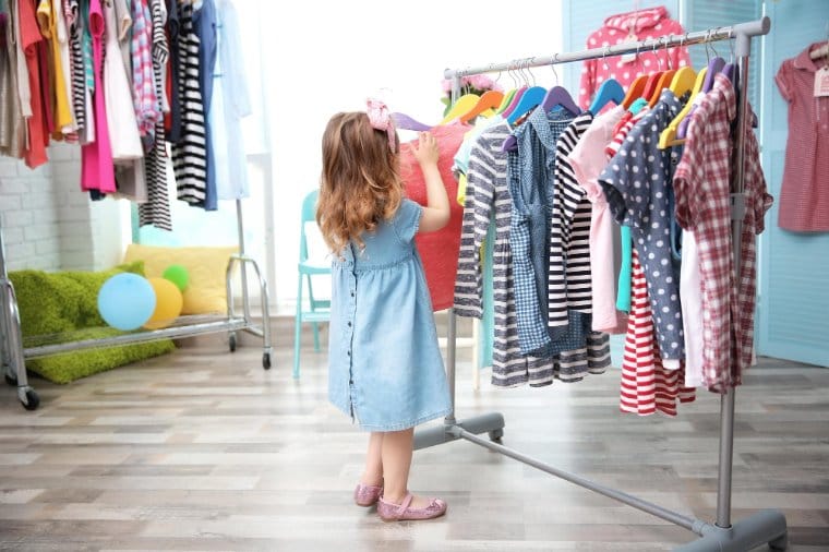 Little girl going through a rack full of different clothes