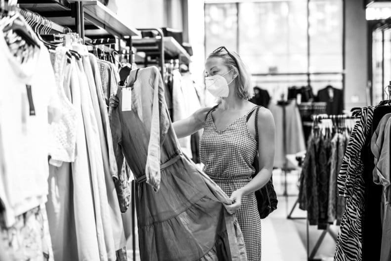 Woman wearing face mask carefully examining dress on rack