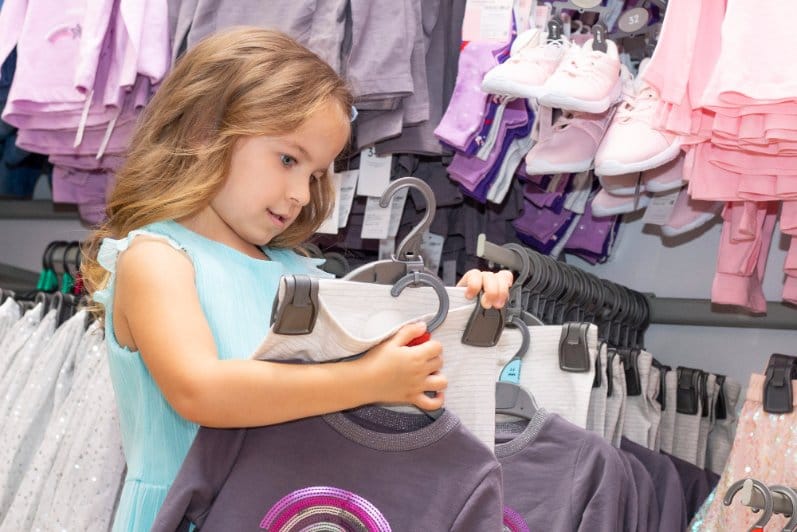Little girl checking out different outfits in a clothing store