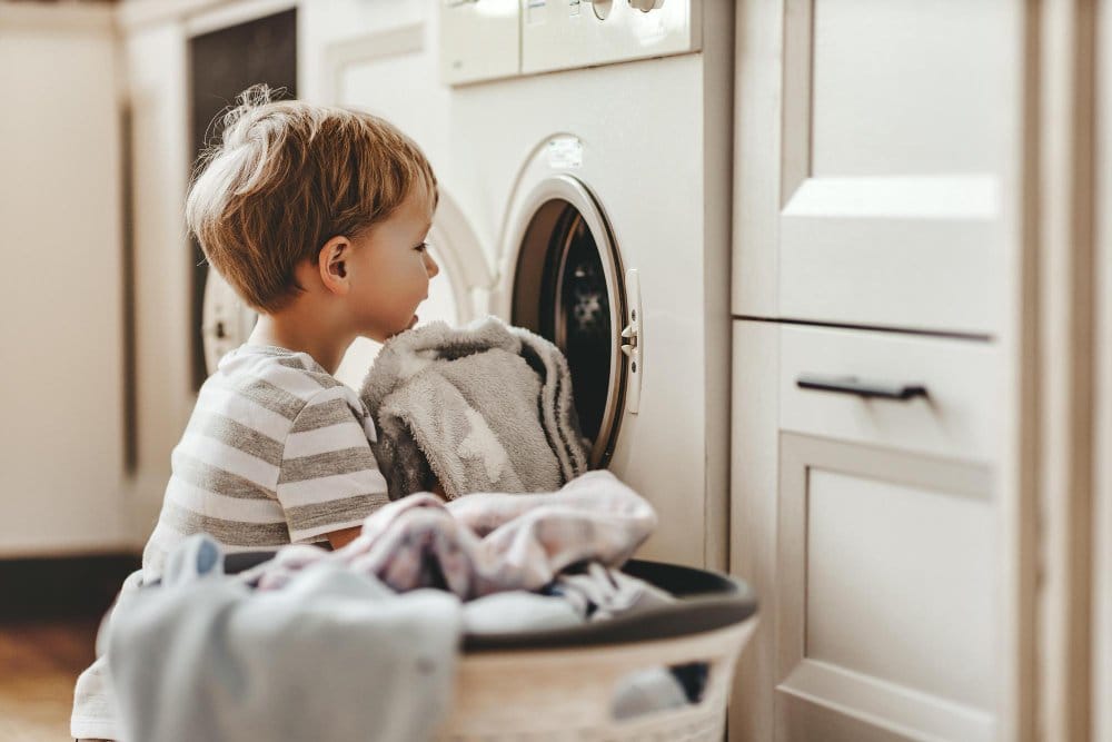 Happy little boy in front of a washing machine with clothes
