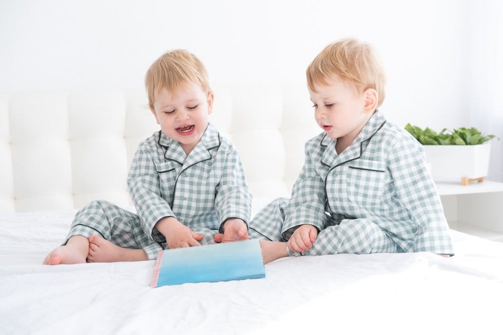 Two happy little twin brothers in pajamas reading a book
