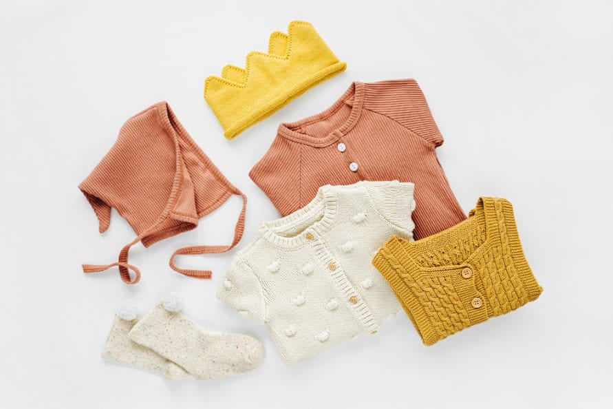 Set of toddler rompers, hat, socks and knitted jumper on white bed