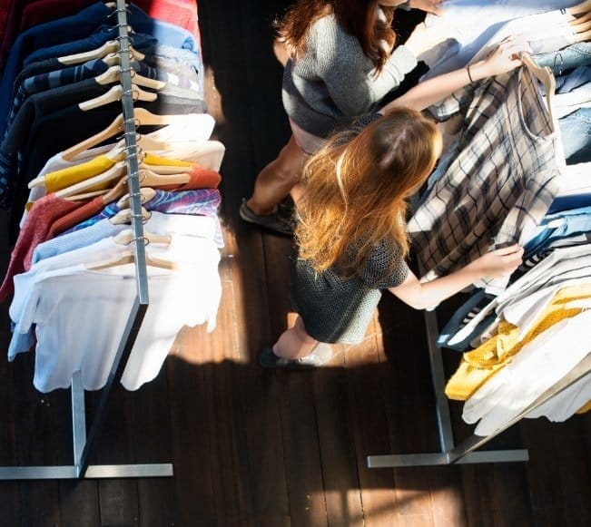 Two women browsing clothing racks during busy shopping trip