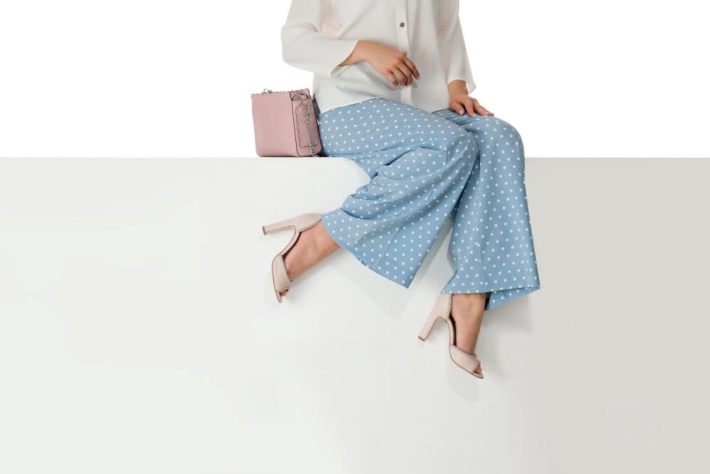 A woman wearing wide leg pants with high heels sitting on bench