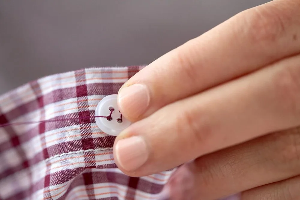 Close up of shirt button being checked for loose threads